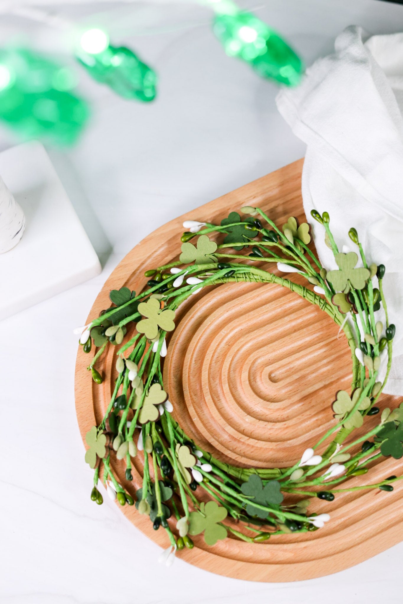 Wooden Shamrock Candle Ring displayed on wooden tray with green shamrock leaves and white floral accents in soft light