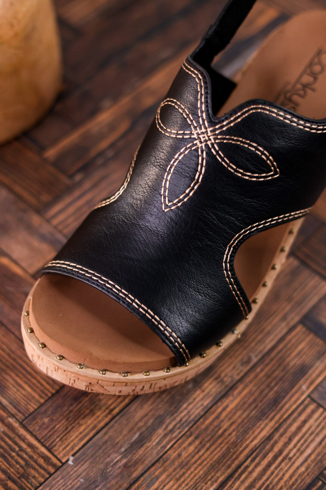 Black Faux Leather Wedges With Stitching featuring floral-inspired stitch detail and studded cork wedge on wooden floor background