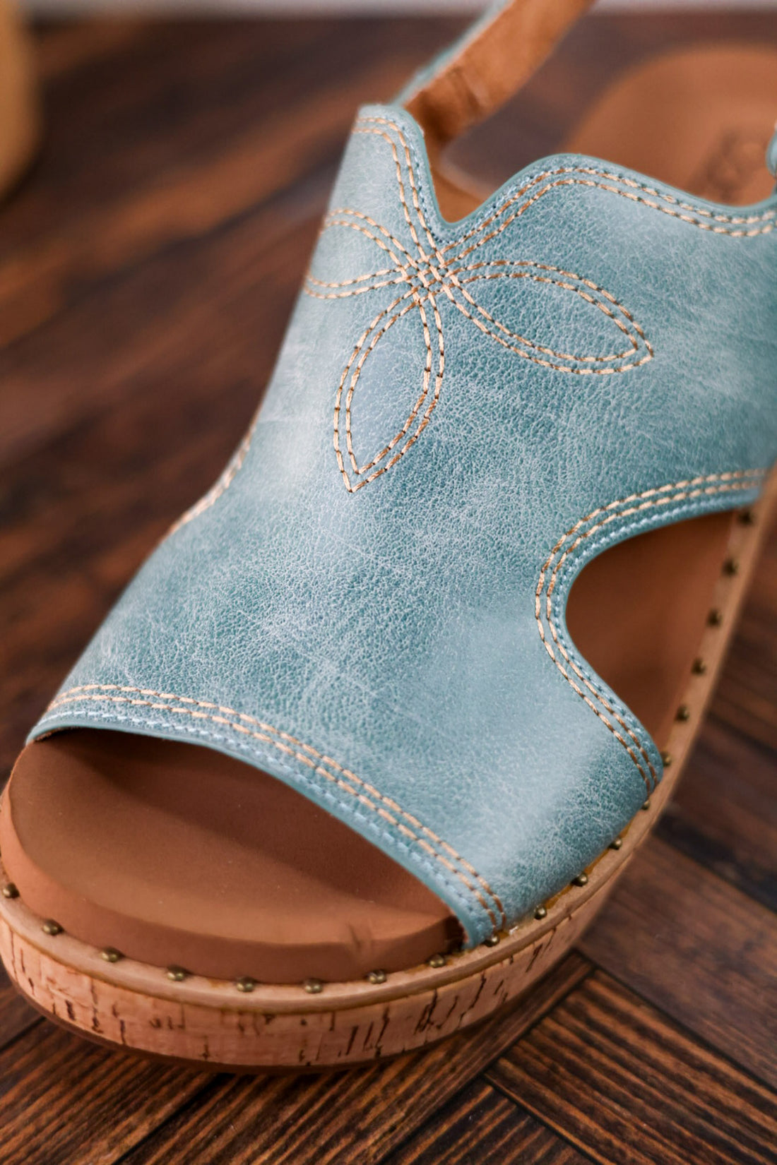 Turquoise Faux Leather Wedges With Stitching showing detailed floral stitch and cork sole on wooden floor background