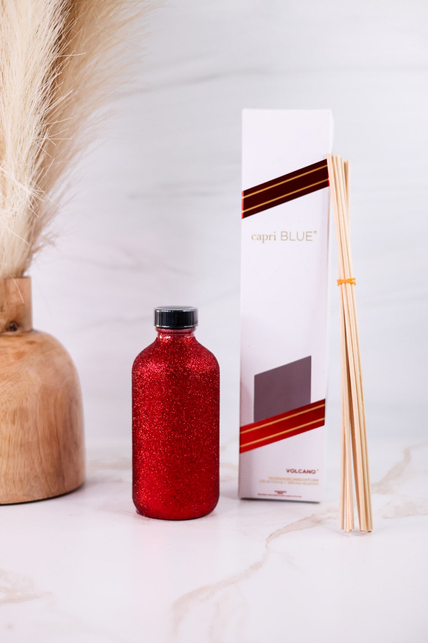 Red Glitter Reed Diffuser With Volcano By Capri Blue with diffuser sticks and sleek white and red packaging on marble surface