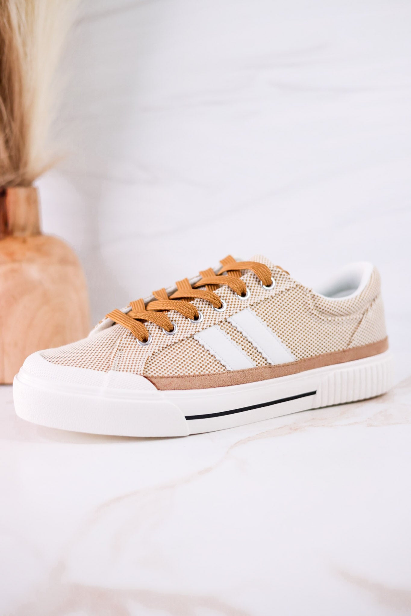 That's Her Tan Tweed Sneakers with white stripes and brown laces displayed on a light marble surface with a wooden vase behind