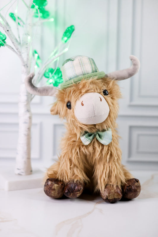 Lush St. Patrick's Day Highland Cow Tabletop Sitter wearing plaid hat and bow tie on white marble surface