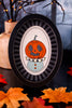 Halloween-themed pumpkin decoration in a black frame with autumn leaves and lights in the background.