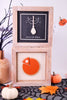 Two framed artworks on a Halloween-themed table with pumpkins and leaves.