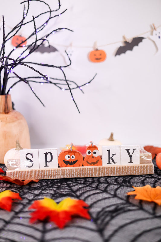 Halloween-themed decor with 'Spooky' sign, pumpkins, and leaves on a spiderweb background.