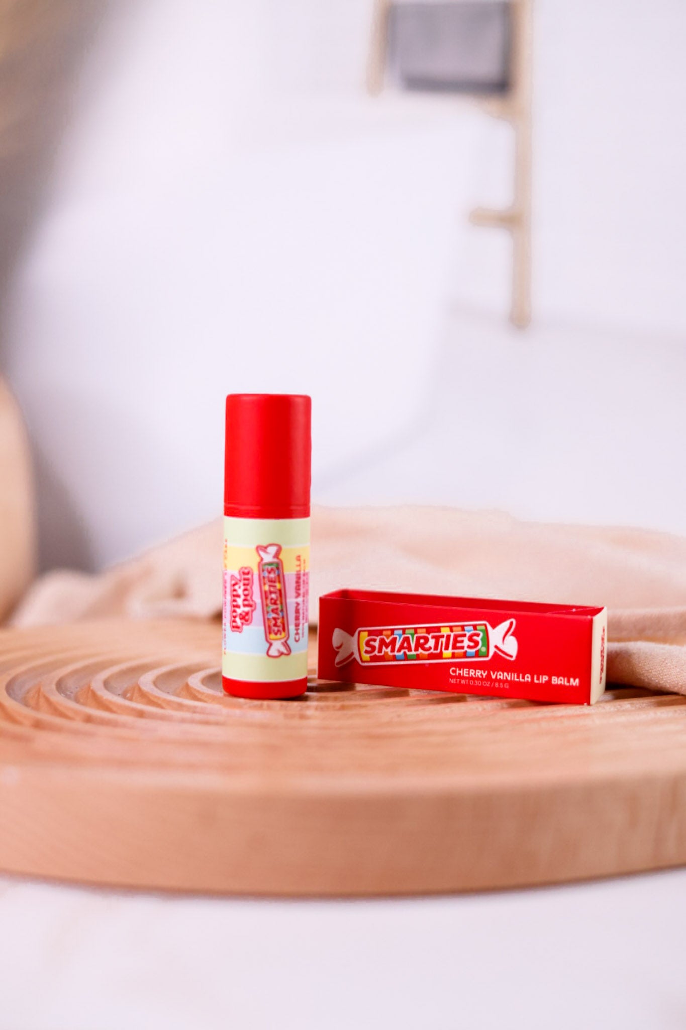 Smarties Lip Balm with cherry vanilla flavor displayed on round wooden tray with soft neutral background