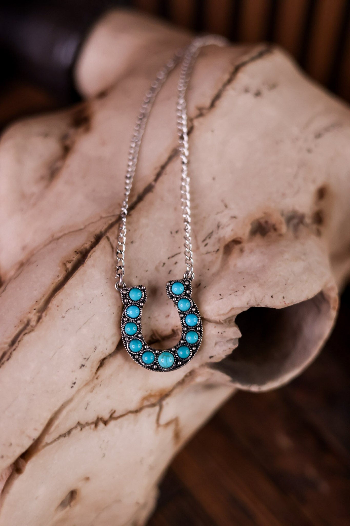 Western Style Horseshoe Pendant Necklace With Turquoise Stones displayed on rustic animal skull background