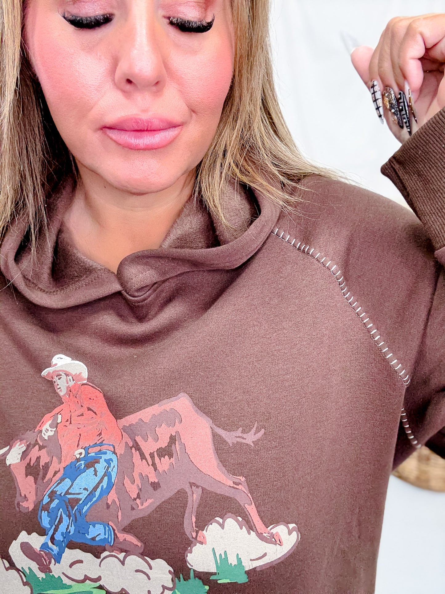 Close-up of woman wearing Western Bullrider Hoodie In Chocolate Brown with detailed graphic and stitched seams