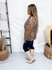 Side view of woman wearing Leopard Print Long Sleeve Mesh Henley Top paired with dark jeans and white boots indoors