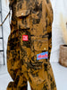 Close-up of Brown Cow Camo Print Cargo Pants With Western Patches featuring pockets and embroidered patches in neutral setting