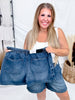 Woman smiling holding Judy Blue High Waist Featherweight Shorts With Drawstring Tie in faded denim indoor setting