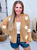 Smiling woman wearing Knit Cardigan with Daisies in Camel Brown paired with white tank top and denim shorts in cozy setting