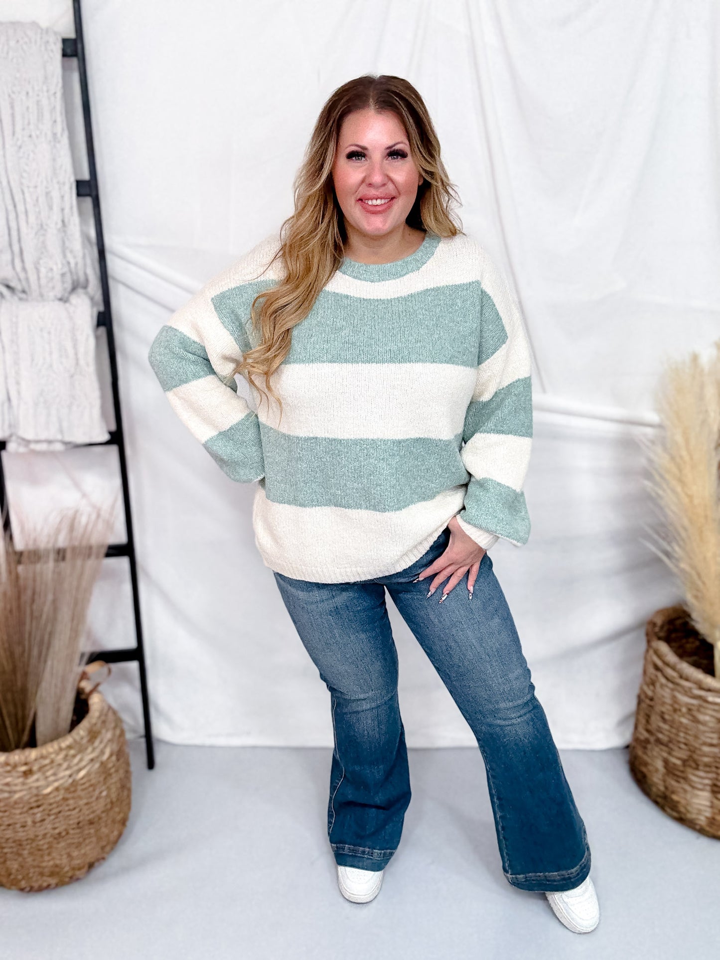 Plus size woman wearing Sage & Cream Striped Soft Knit Long Sleeve Sweater with blue jeans in bright studio setting