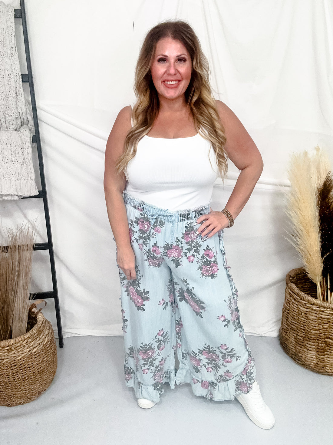 Plus size woman smiling wearing Light Blue Floral Chambray Pants With Ruffled Hem and white tank top indoors