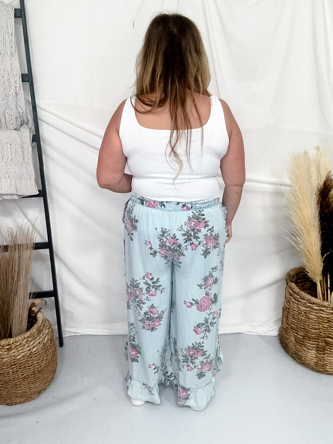Back view of plus size woman wearing Light Blue Floral Chambray Pants With Ruffled Hem in relaxed fit indoors