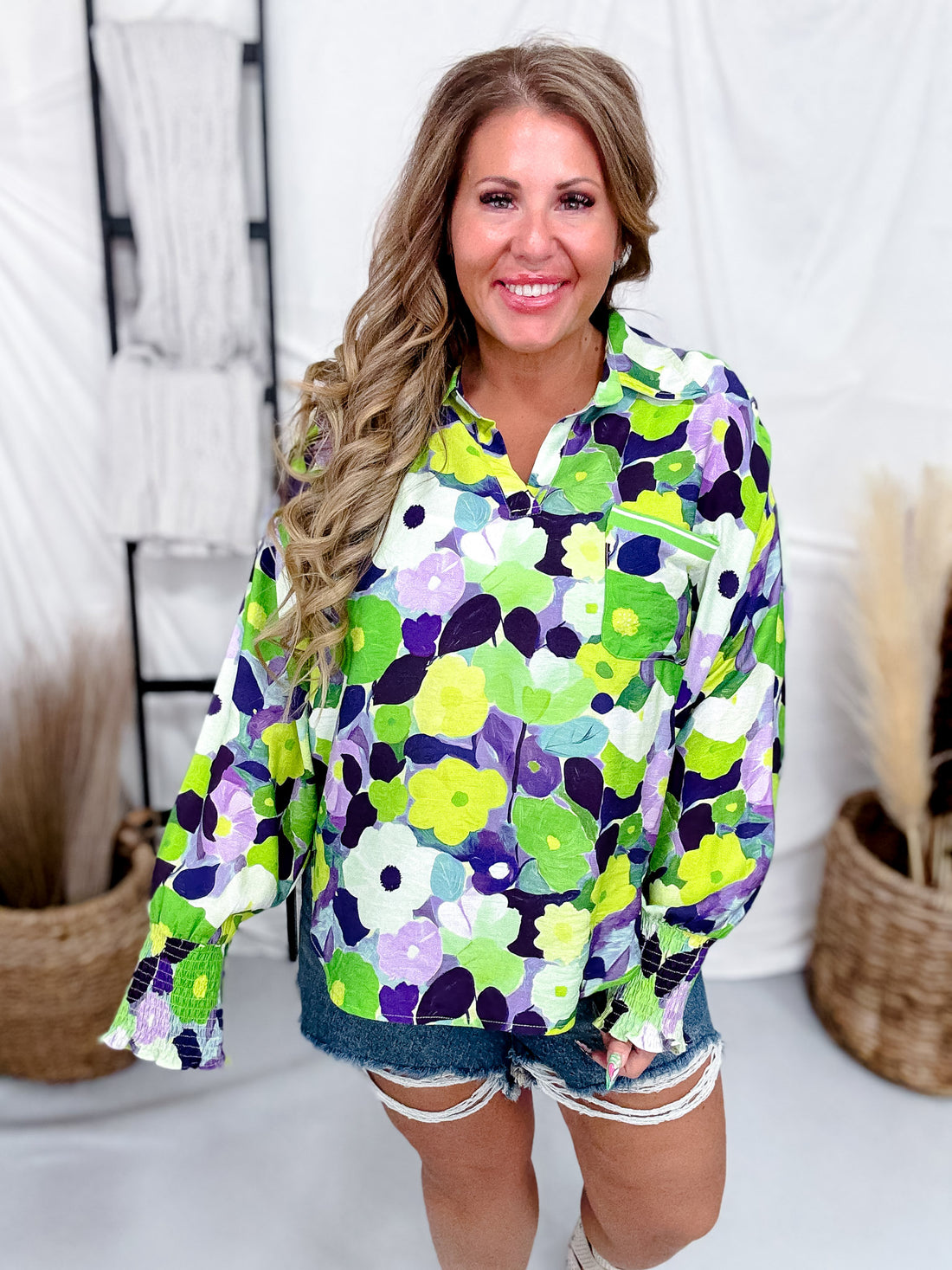 Woman modeling Green & Purple Floral Print Button Down Top with long sleeves and relaxed fit paired with denim shorts indoors