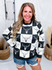 Woman smiling wearing Black & White Checkered Cow Skull Print Sweater styled with ripped denim shorts indoors
