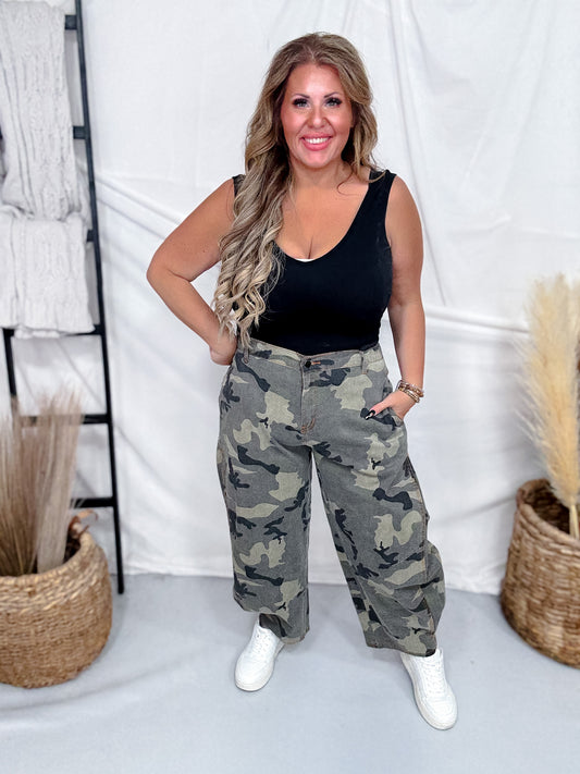 Woman wearing Olive & Gray Camo Print Cropped Barrel Leg Pants styled with black tank top and white sneakers