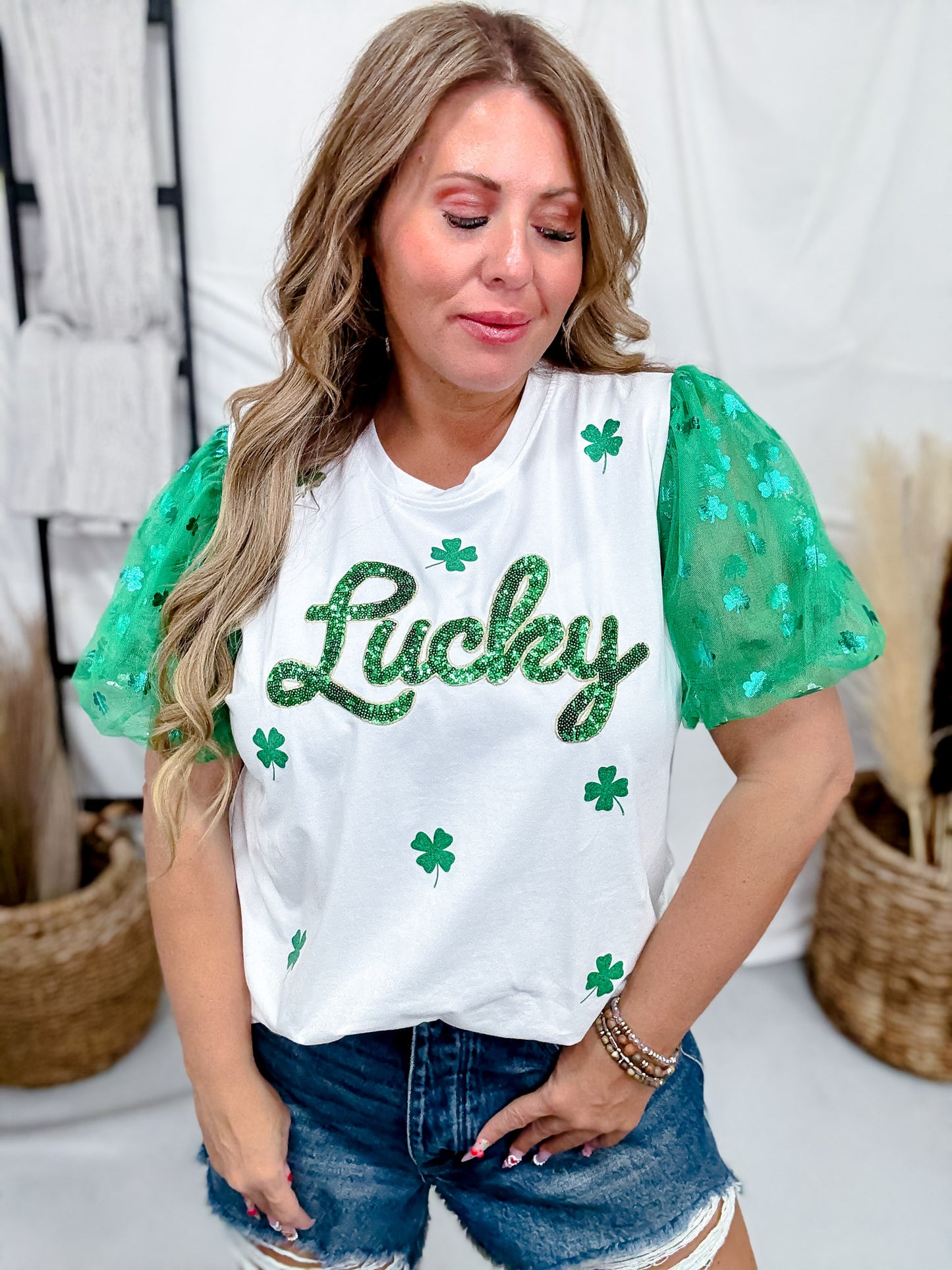 Woman wearing Sequined "Lucky" Top With Tulle Sleeves featuring green shamrocks and paired with denim shorts indoors