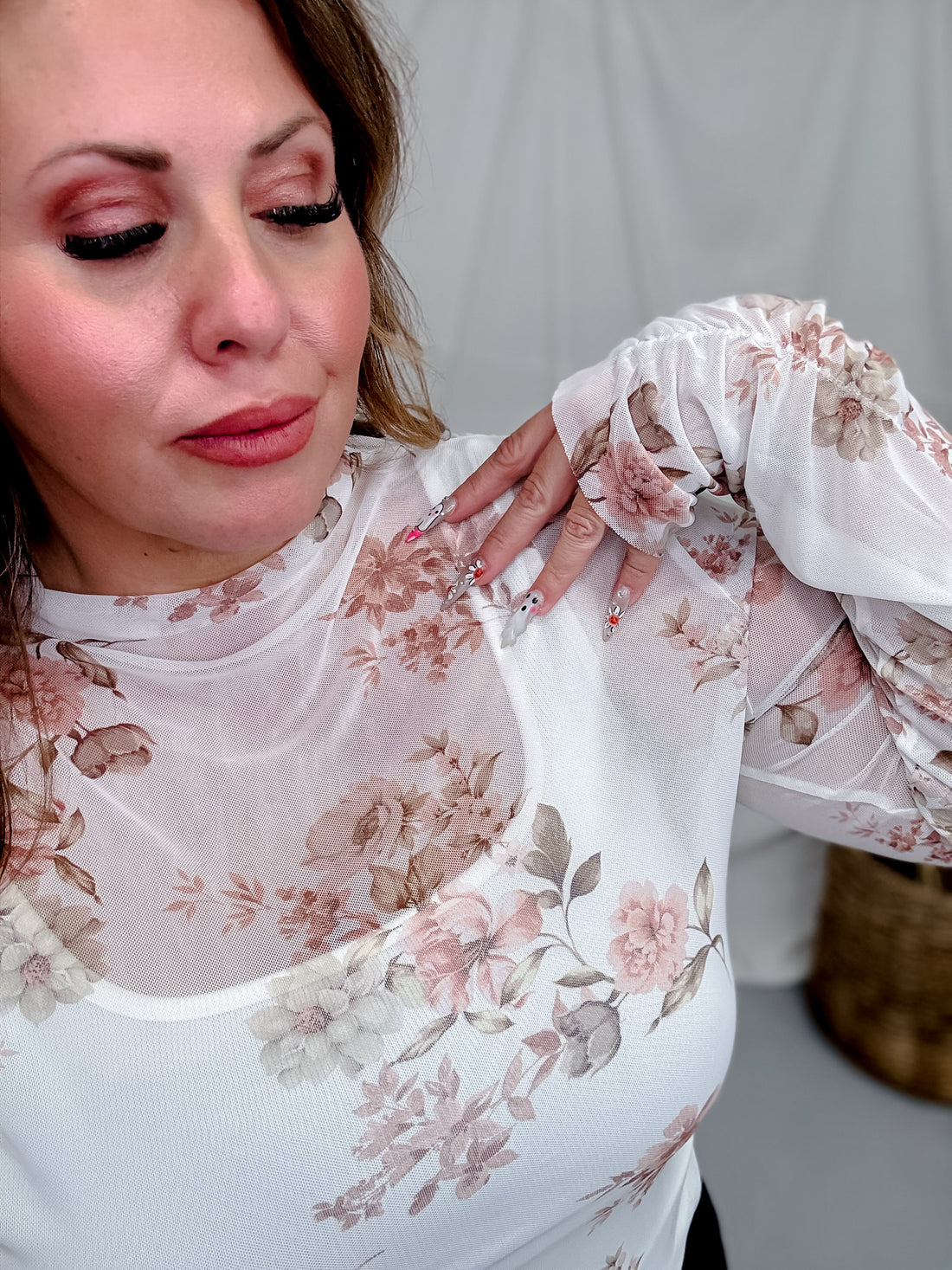 Close-up of woman wearing Ivory & Taupe Floral Print Long Sleeve Mesh Top with floral nails in soft neutral setting